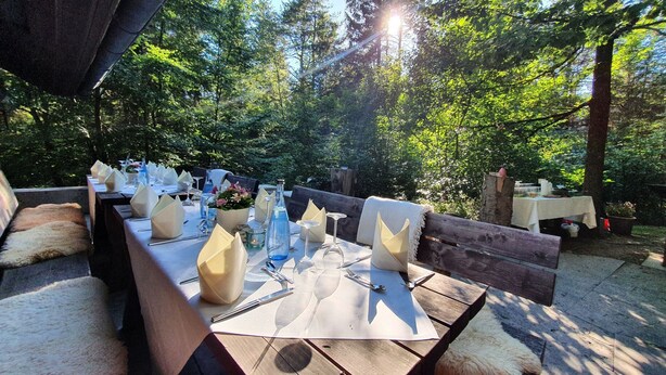 An outdoor dining area with wooden tables and benches, surrounded by trees. - Speidel's Brau Manufaktur (Hohenstein)