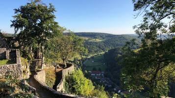 A historic stone wall with a staircase leading to a higher vantage point, overlooking a valley with houses and a river.