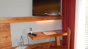 Ein Hotelzimmer mit einem Holztisch, einem an der Wand montierten Fernseher, einem roten Vorhang und einem Fenster mit Jalousien.