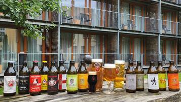 Een rij bierflesjes en glazen op een houten tafel voor een gebouw met meerdere balkons.