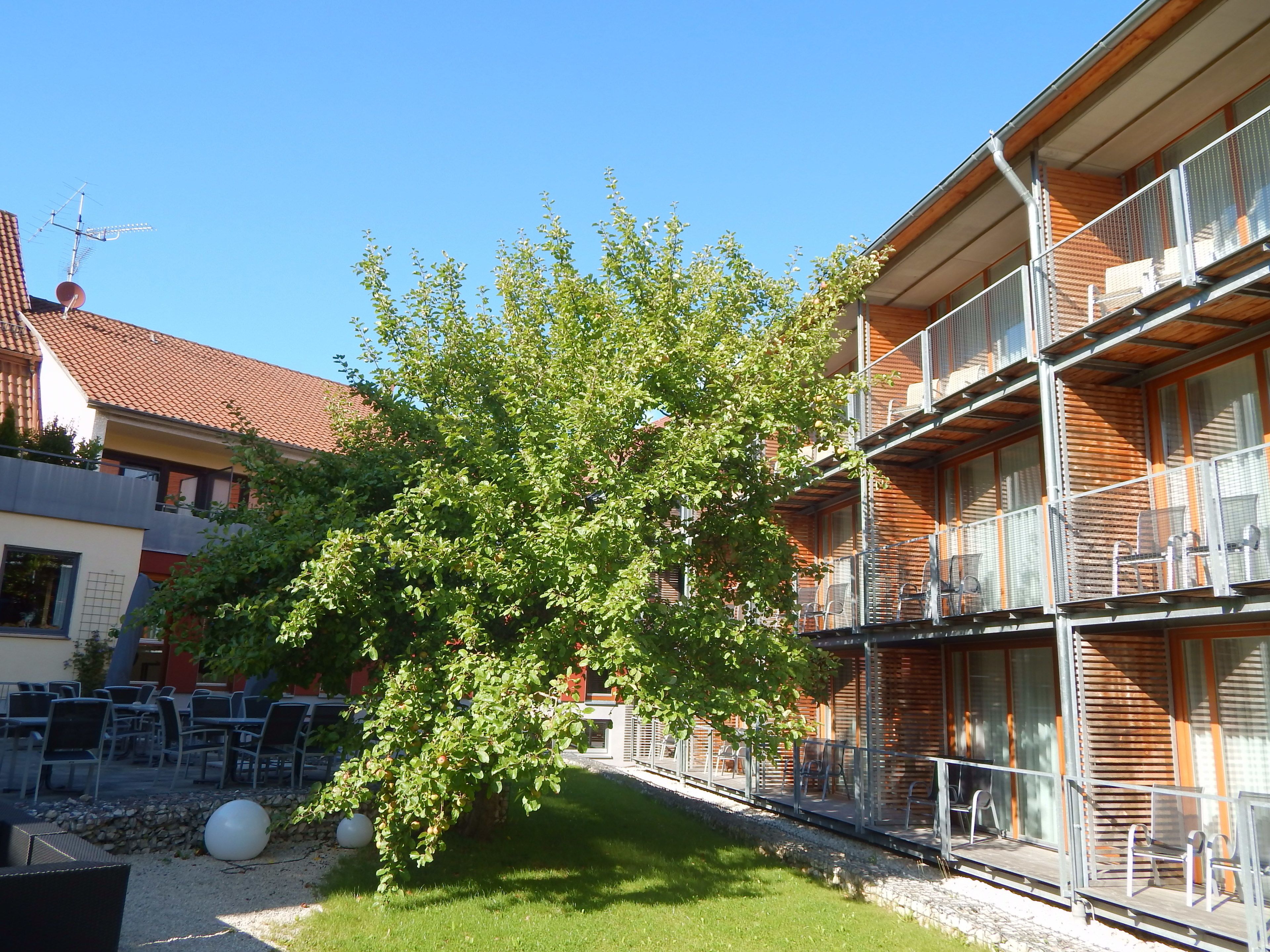Ein Gebäude mit Balkon, Außenbereich und einem Baum davor.