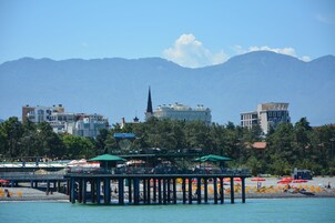 A pier with umbrellas and beach chairs, a mountain in the background, and buildings with a church spire.