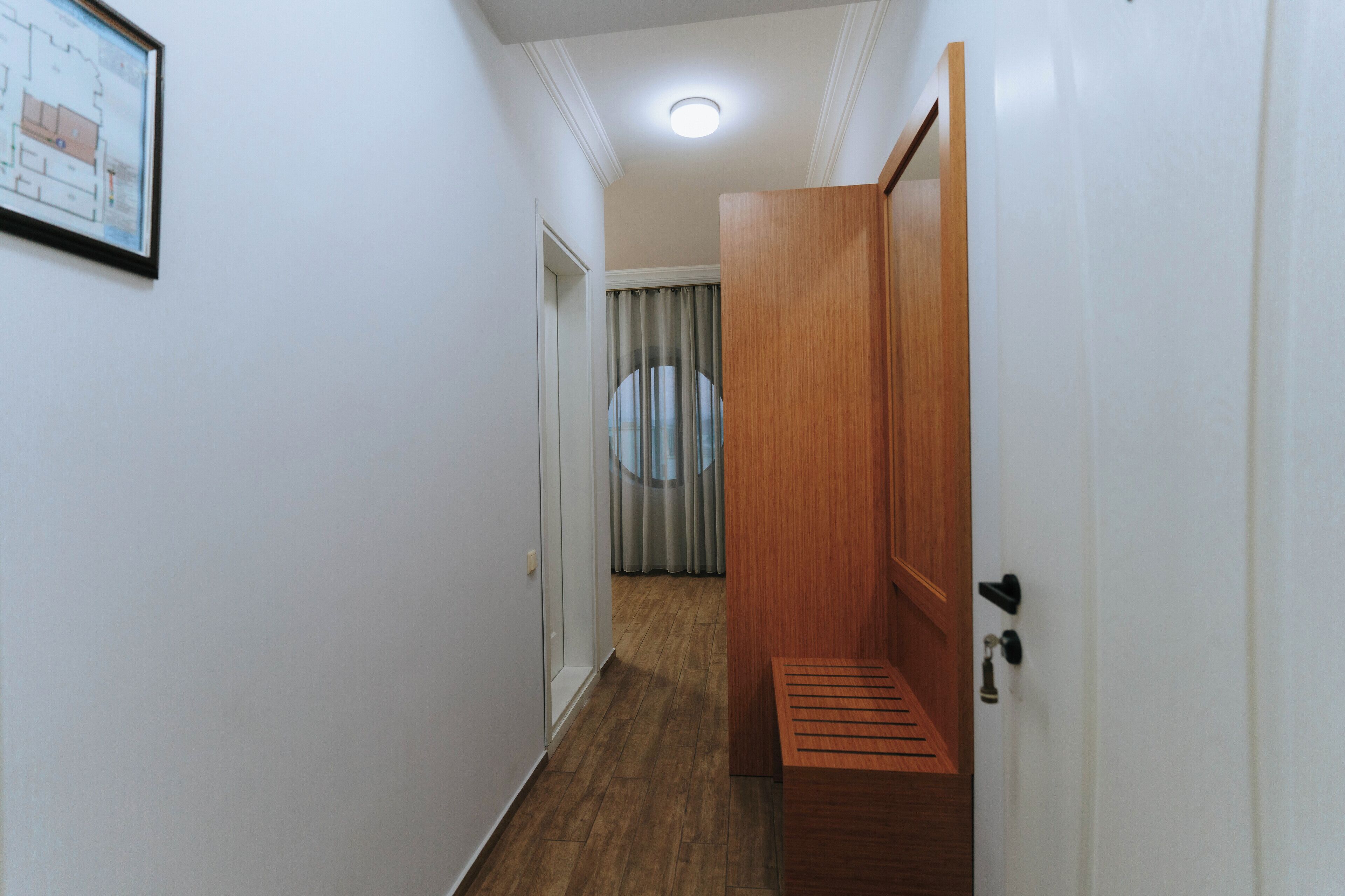 Ein schmaler Flur mit einer hölzernen Bank, einer Tür mit Schlüsselloch und einer gerahmten architektonischen Zeichnung an der Wand.