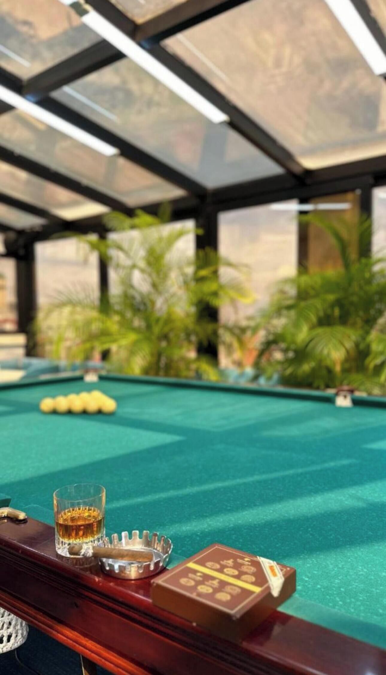 A pool table with a glass of whiskey, a cigar, and a deck of cards.