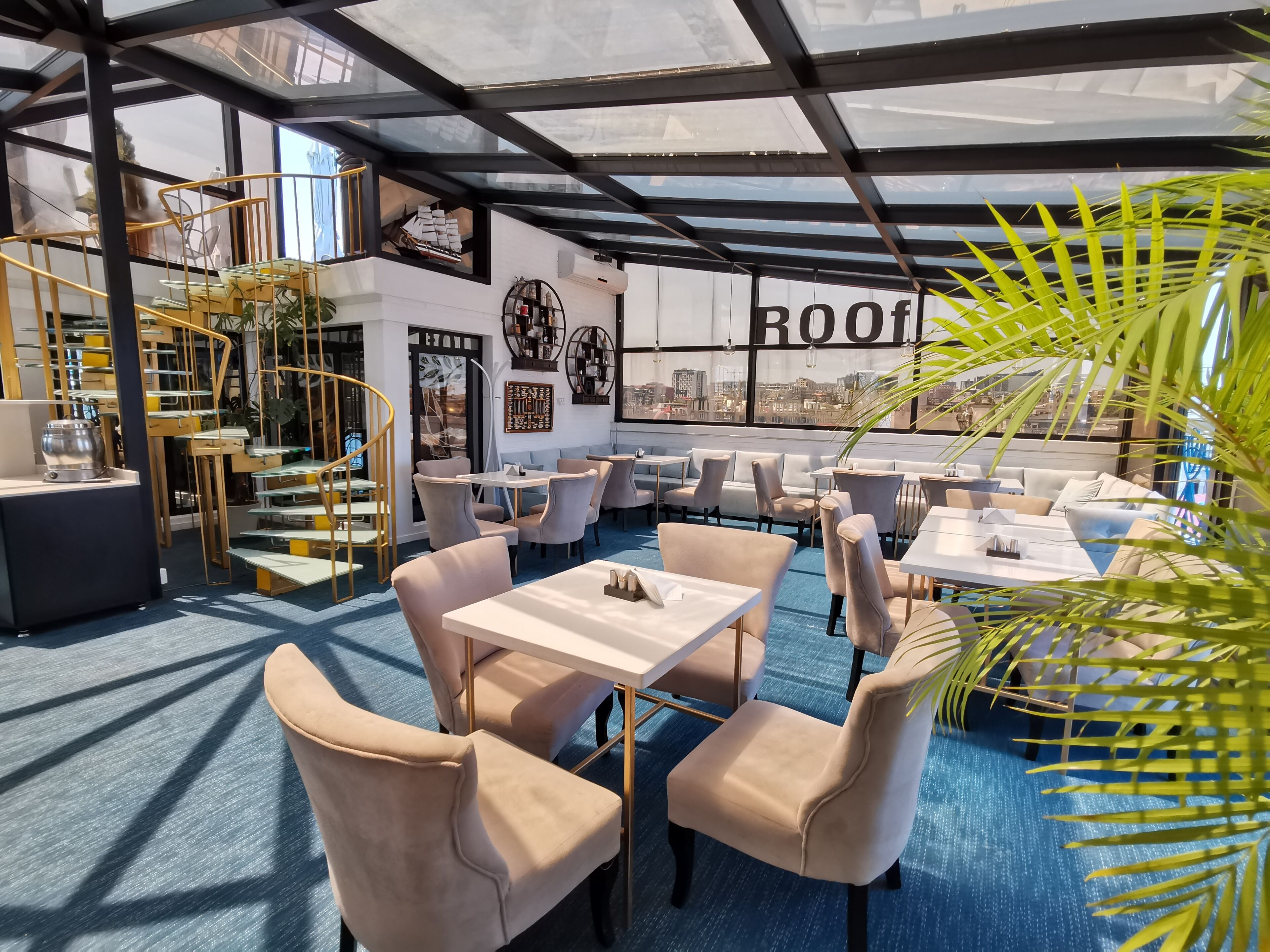 A modern rooftop restaurant with outdoor seating, a spiral staircase, and city views.