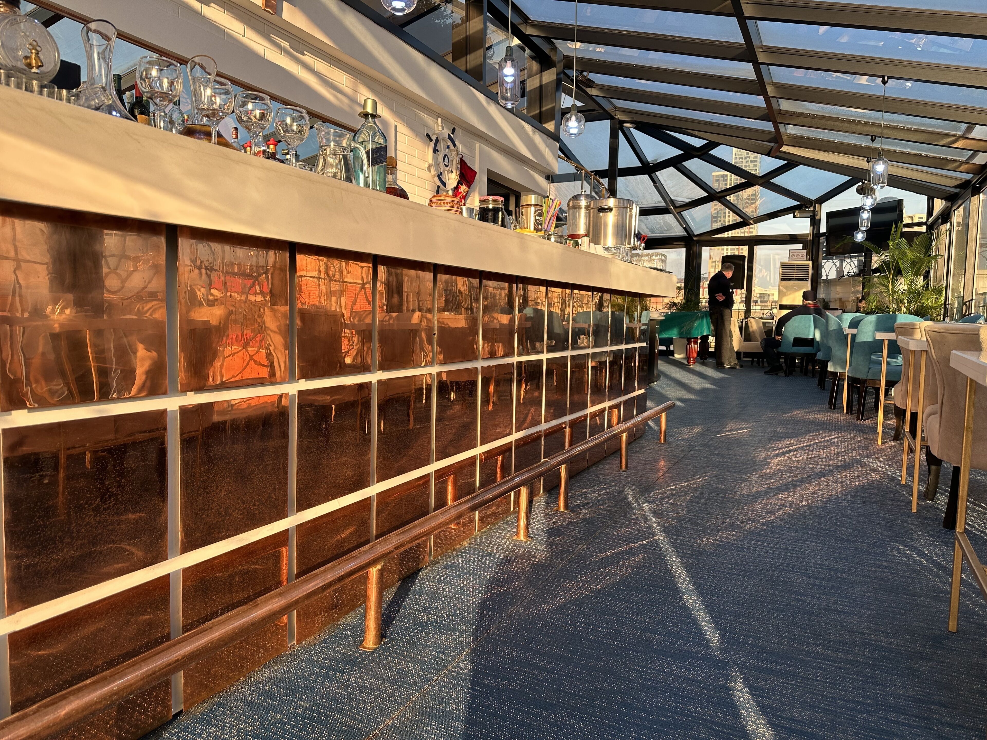 A restaurant with a glass enclosure, tables, chairs, and a variety of glassware and bottles on display.