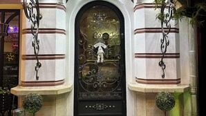 Una entrada negra y ornamentada con un letrero que dice 'WELCOME', una pequeña estatua y dos plantas en macetas.