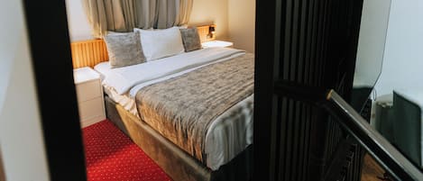 A hotel room with a bed, a nightstand, a lamp, and a television.