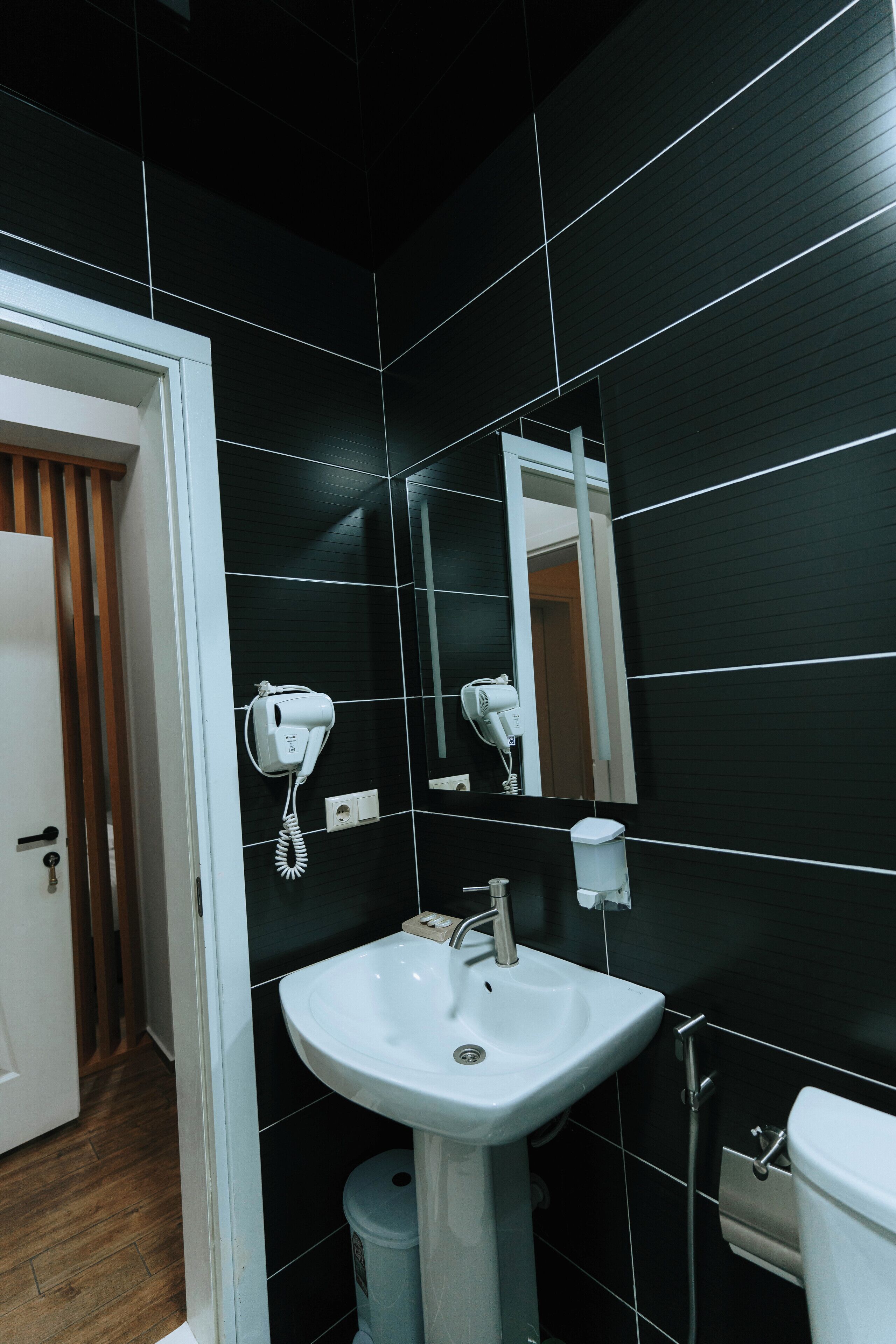 A modern bathroom with black tiled walls, a white sink, a hairdryer, and a mirror.