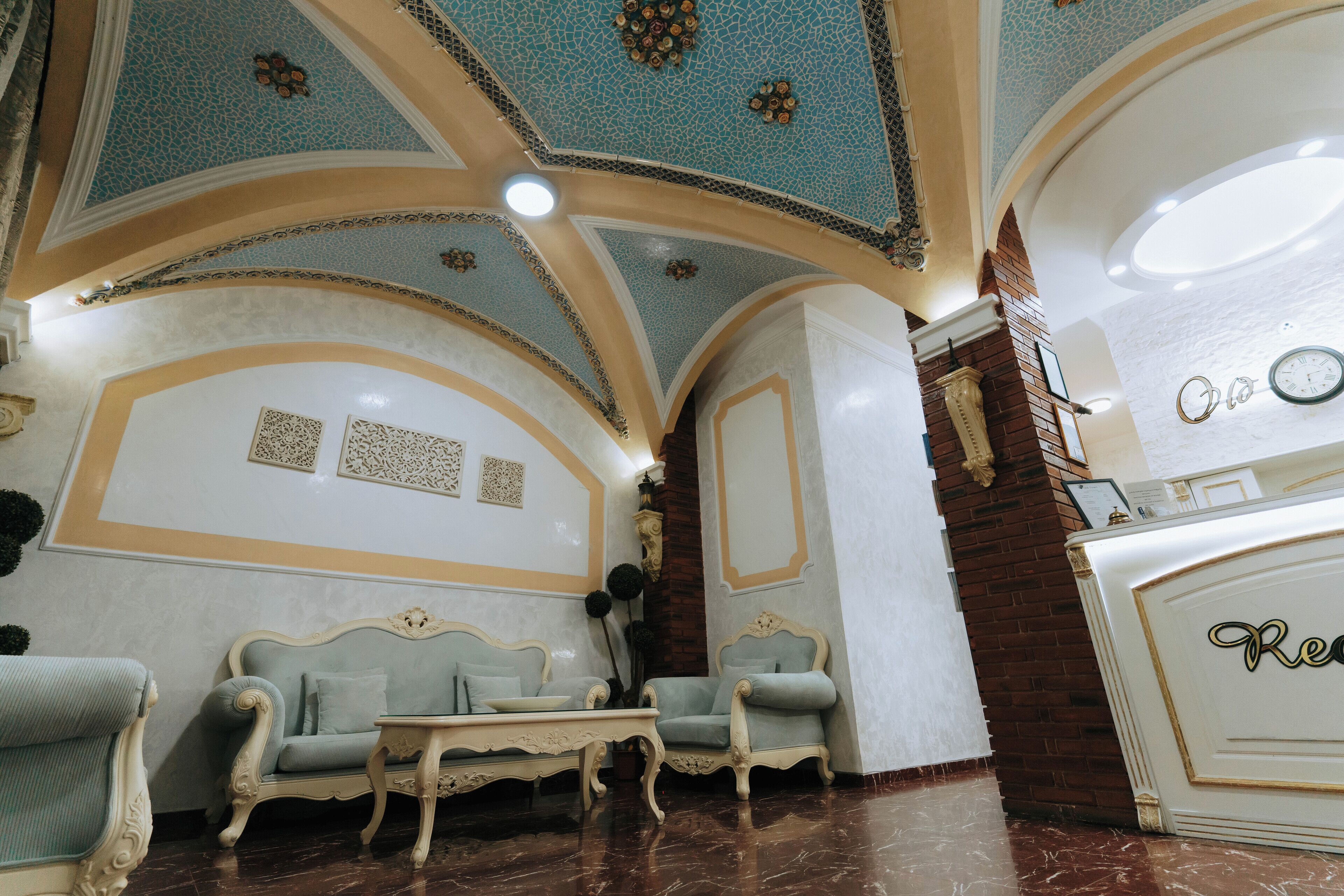 A room with ornate ceiling, two sofas, a small table, and a reception desk.