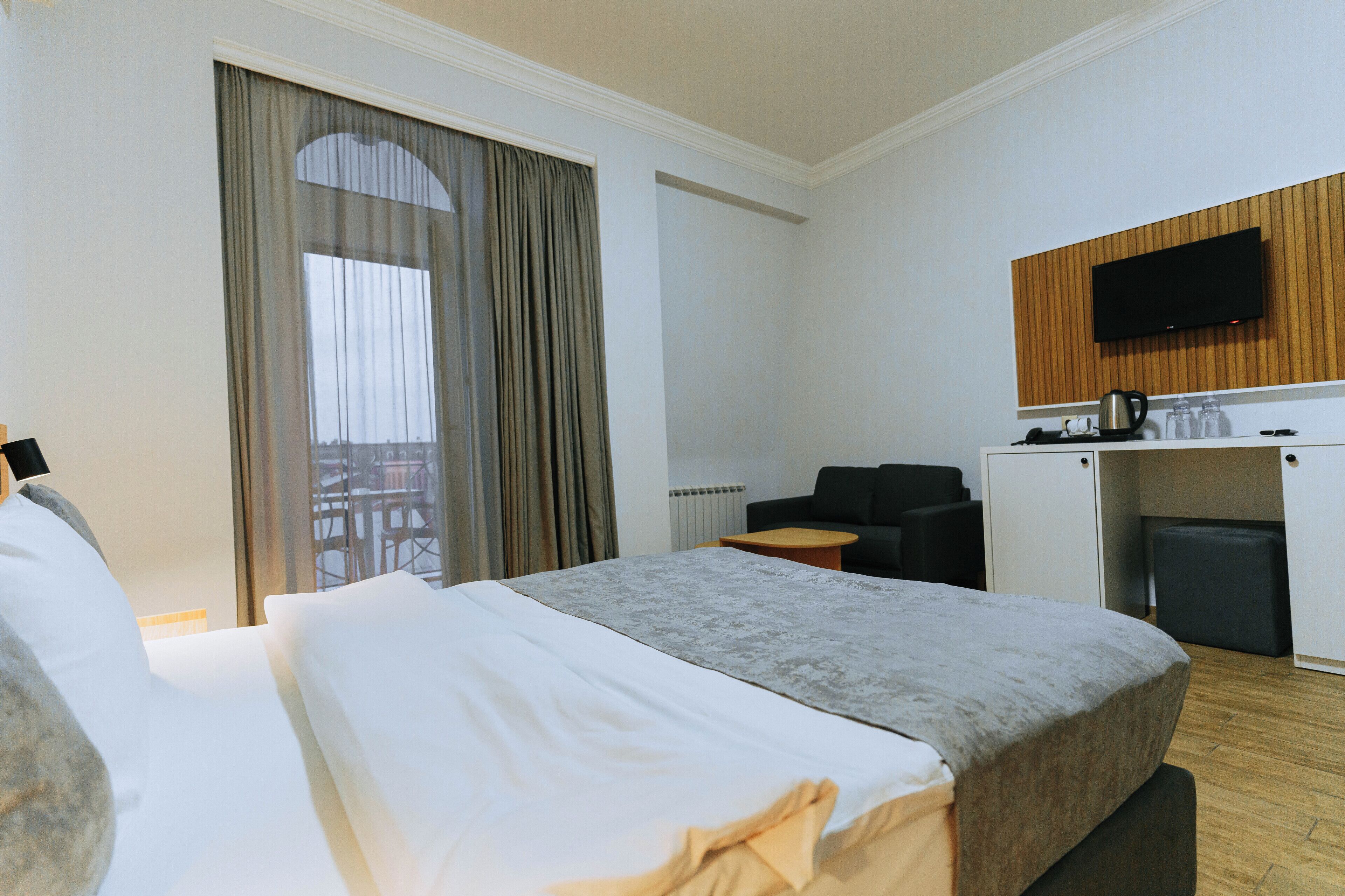 A hotel room with a bed, a desk, a television, and a view of the outdoors.