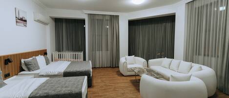 Une chambre d’hôtel moderne avec deux lits, un canapé blanc et un fauteuil blanc.
