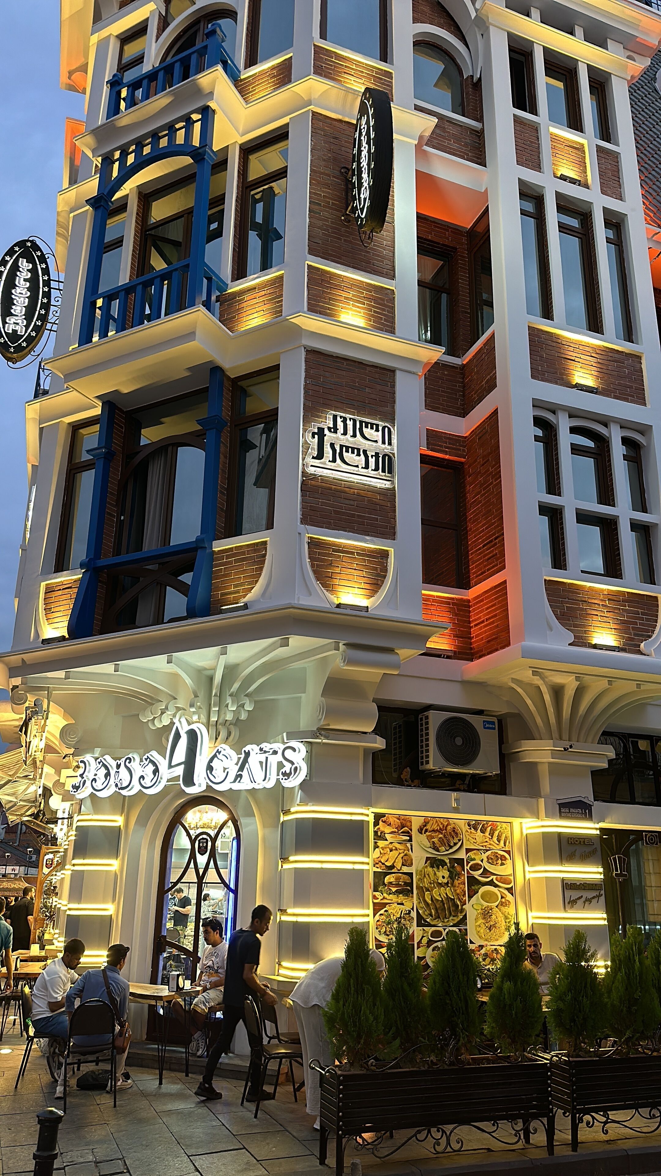 A multi-story building with a restaurant named "BooBoo" on the ground floor, featuring a large illuminated sign and outdoor seating.