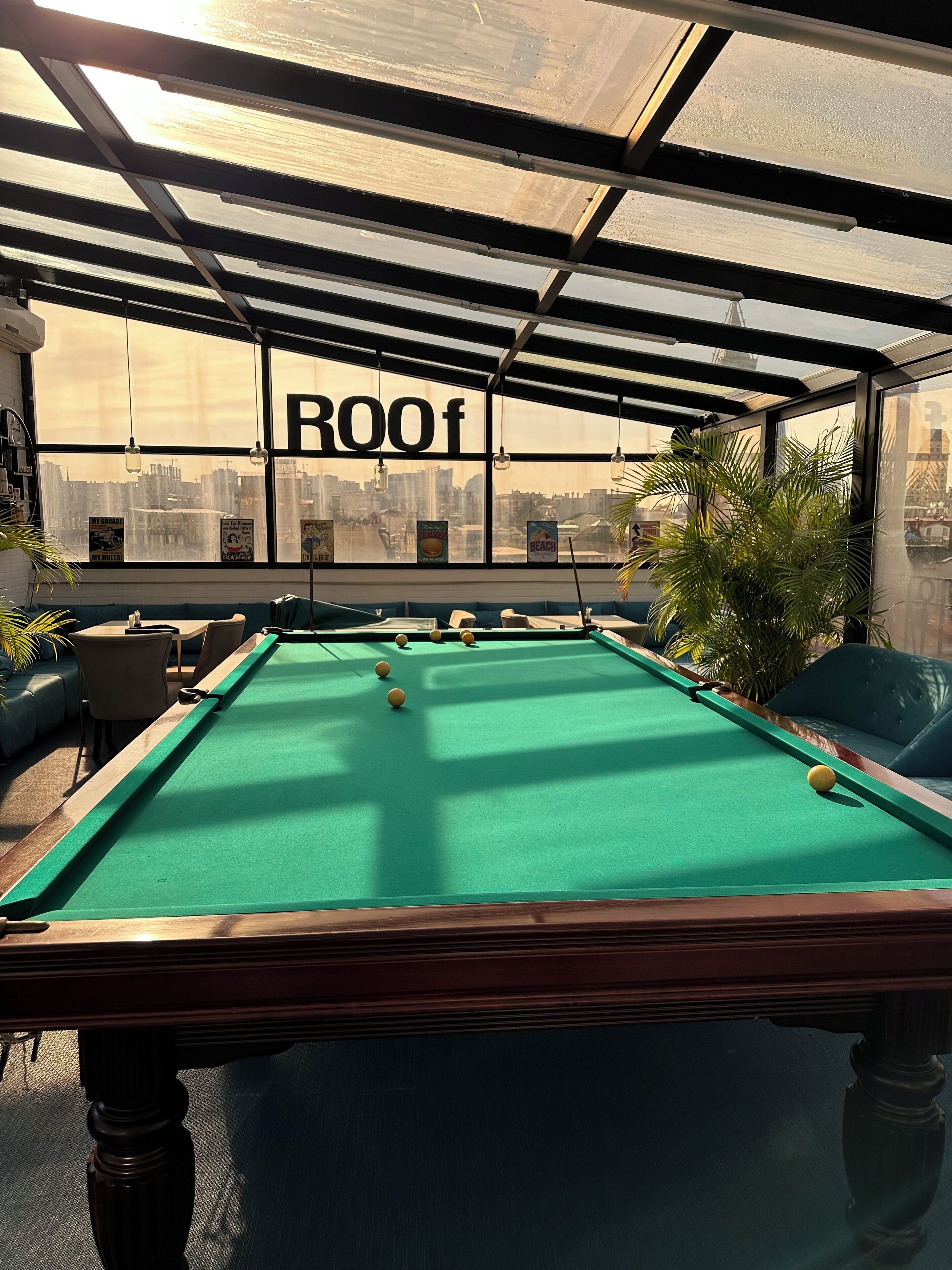 Ein Billardtisch in einem Raum mit Blick auf die Stadt, ein Schild mit der Aufschrift 'ROOF' und ein grünes Sofa.