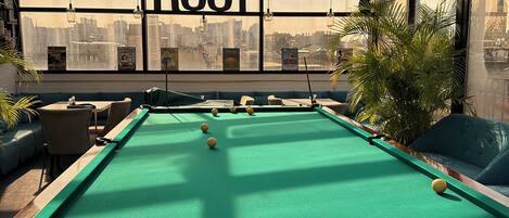 A pool table in a room with a city view, a sign reading "ROOF", and a green sofa.