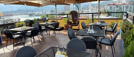 An outdoor terrace with tables and chairs, a view of the city, and a mosque in the background.