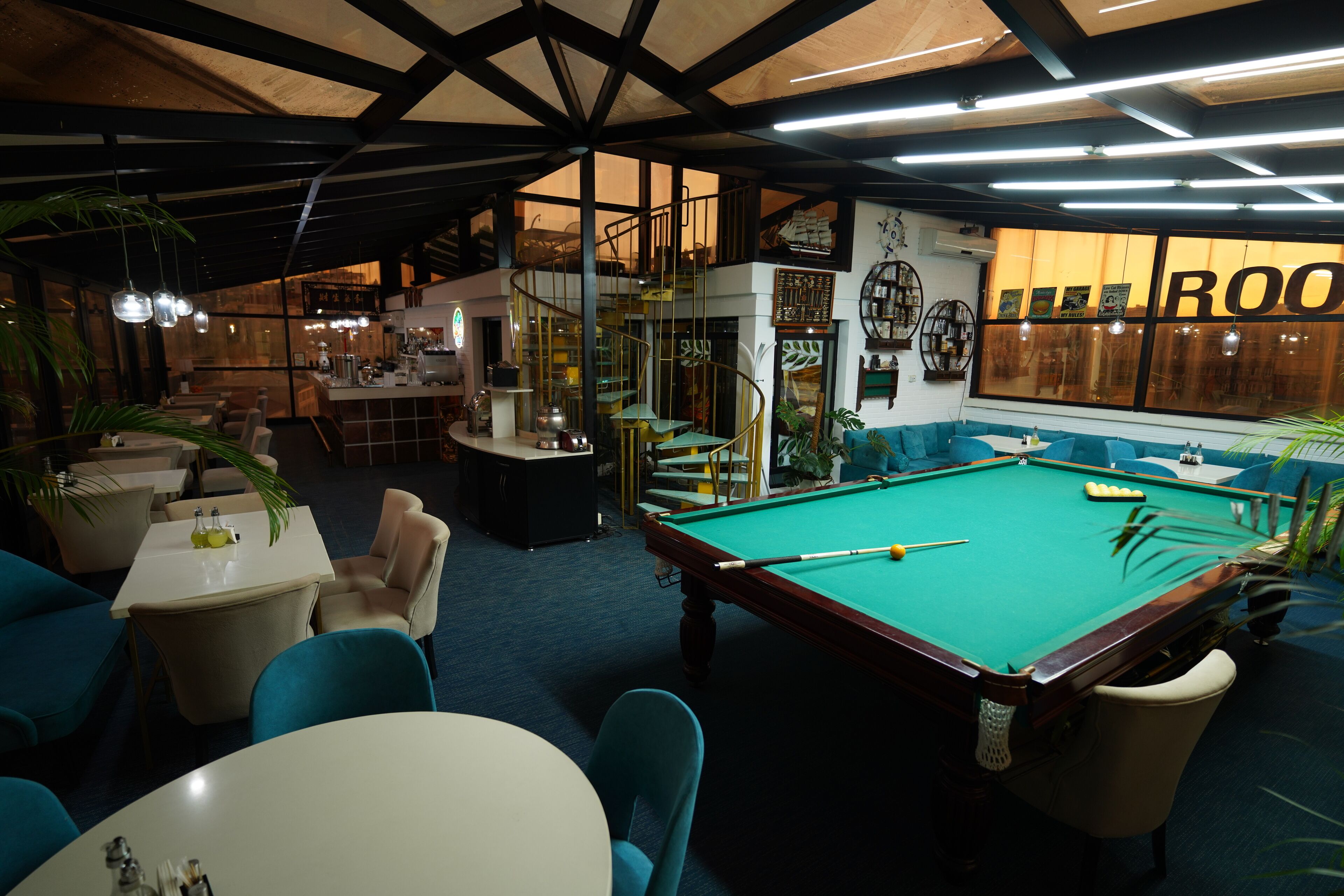 A pool table in a room with blue chairs, a staircase, and a bar area.