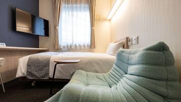Ett hotellrum med en säng, ett skrivbord, en platt-TV och ett stort fönster med gardiner.
