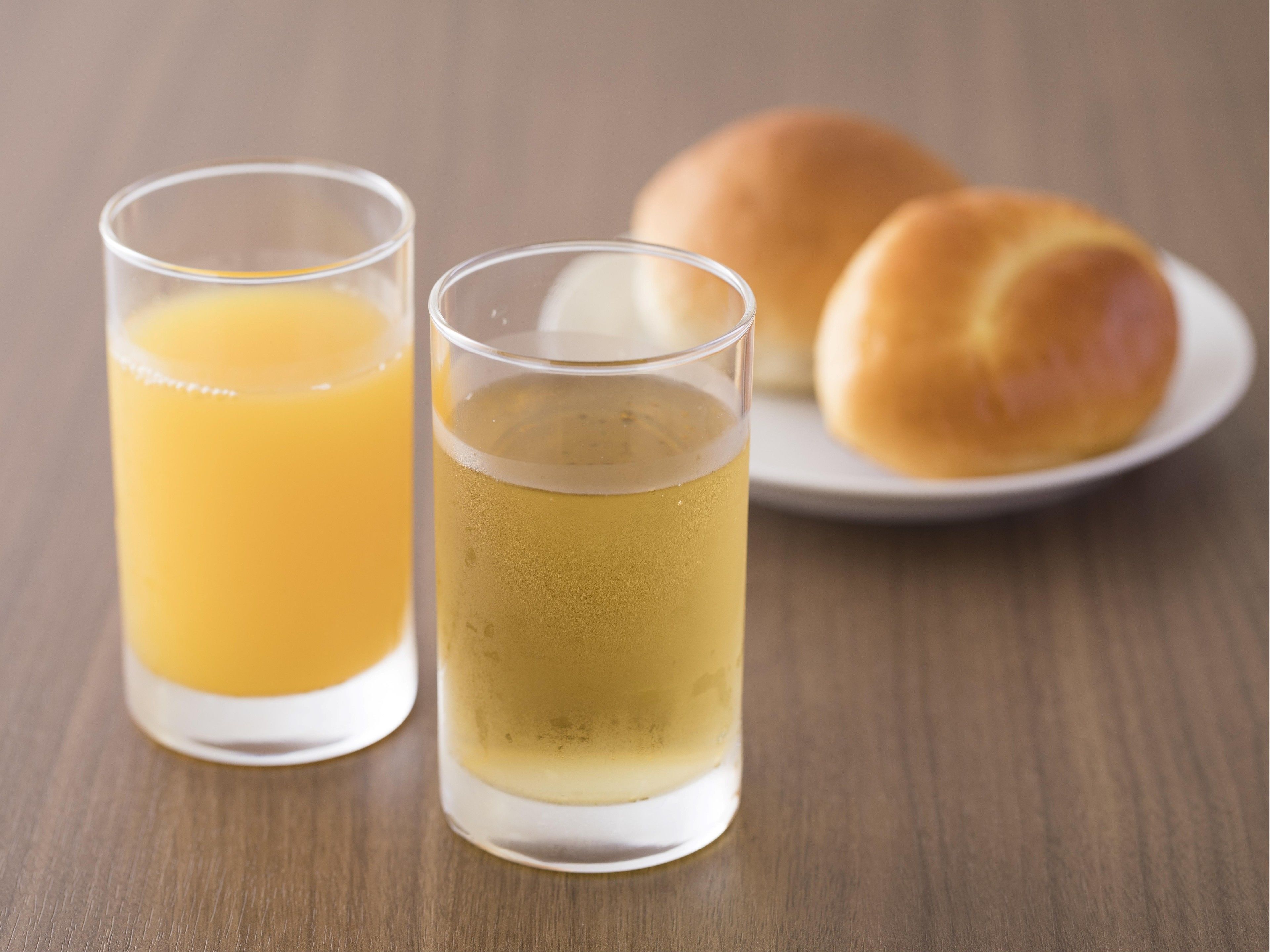 Two glasses of orange juice and a plate with two rolls of bread on a wooden table.