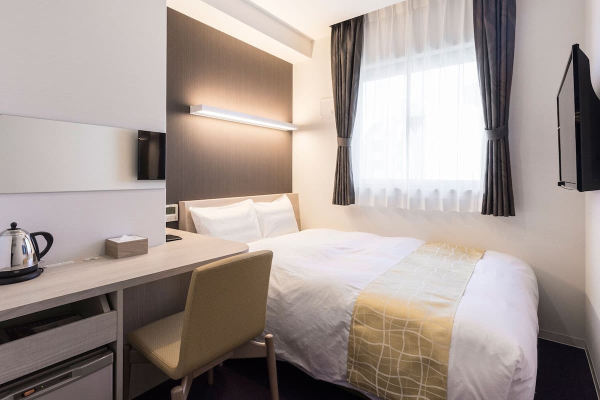 Una habitación de hotel con cama, escritorio, silla, hervidor de agua y televisión.