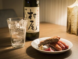 Un verre d’eau, une bouteille de vin et une assiette de saucisses sur une table en bois.