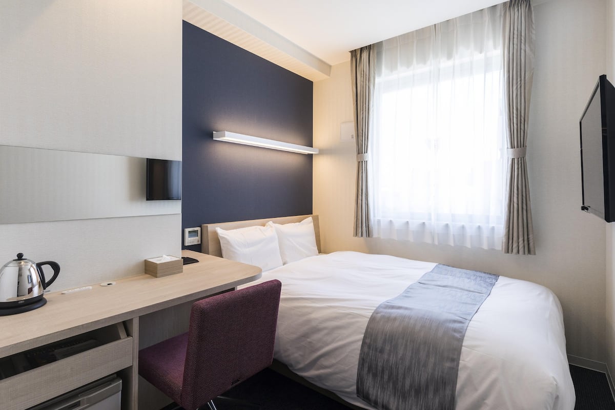 Una habitación de hotel con cama, escritorio, silla, cafetera y televisor.