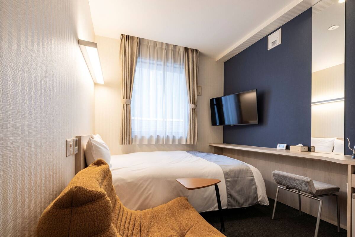 Una habitación de hotel moderna con una cama grande, un escritorio, un televisor de pantalla plana, una silla y una ventana con cortinas.