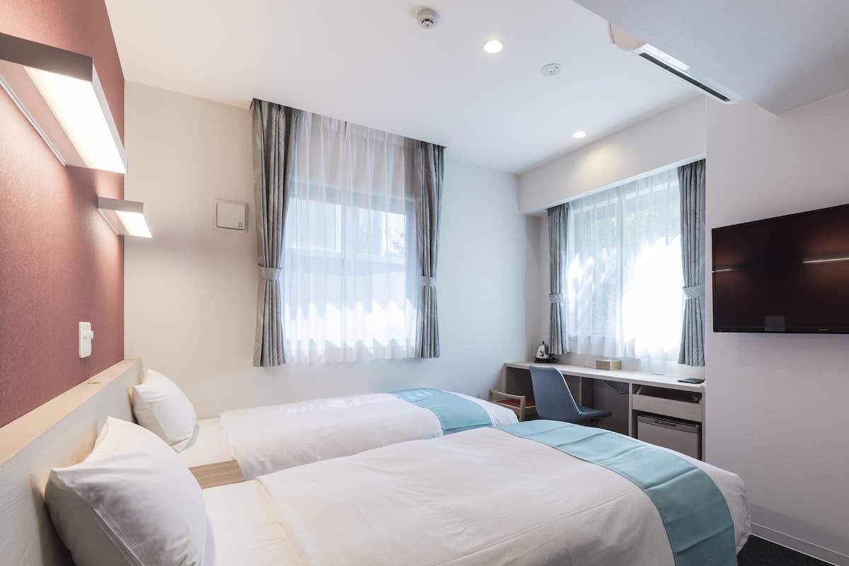 Habitación de hotel con dos camas, un escritorio, una silla, un televisor y una ventana con cortinas.