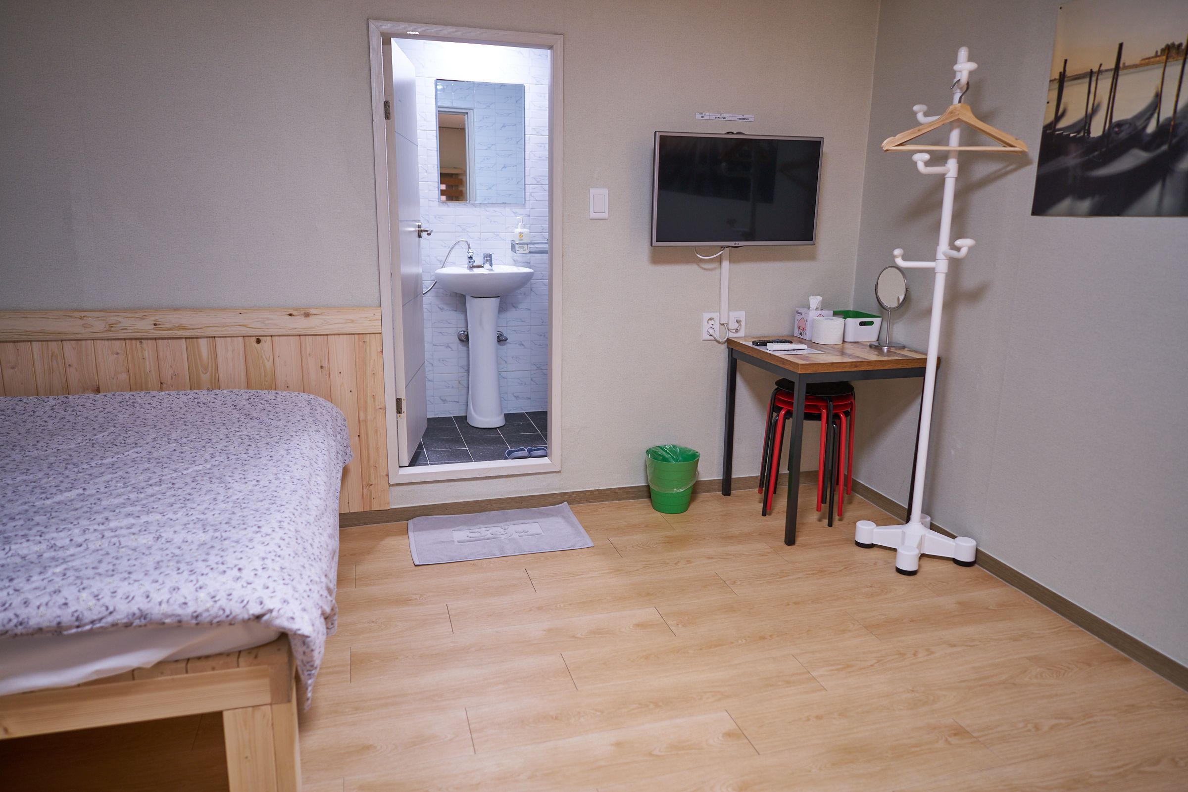 Una camera da letto con un letto, una scrivania con una sedia, una televisione, un appendiabiti e un bagno visibile attraverso una porta aperta.