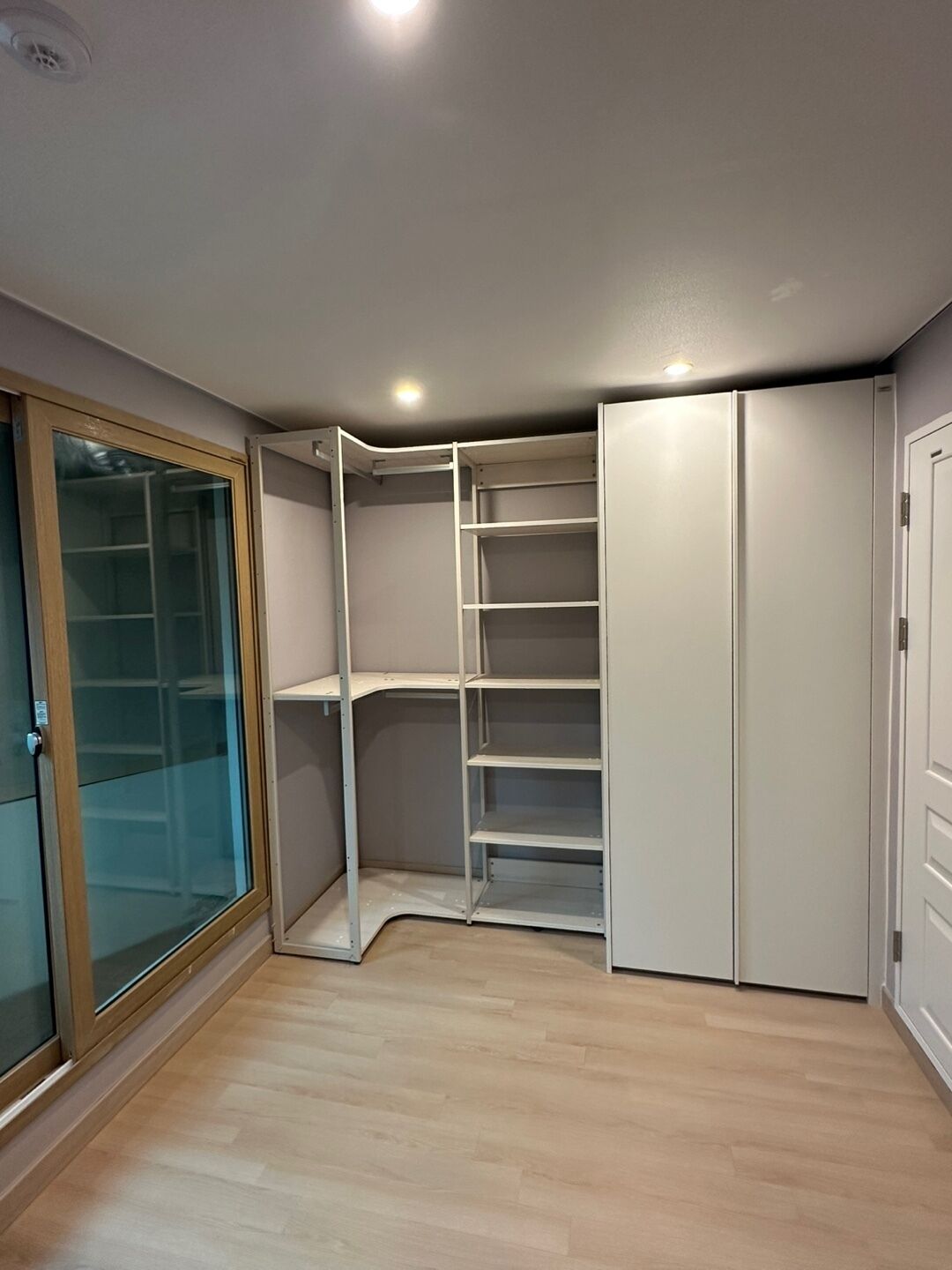 Ein Eckzimmer mit Einbauschrank, Schiebeglasfenster und Holzboden.