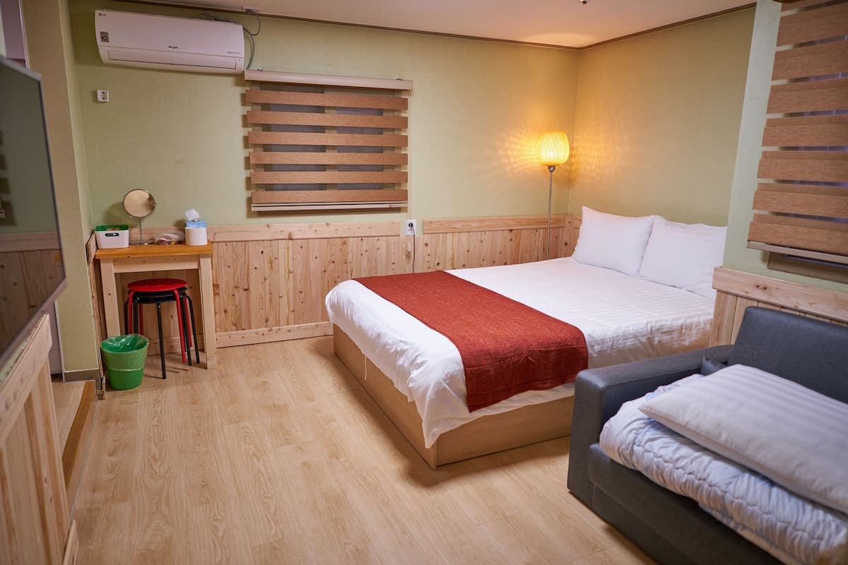 A room with two beds, a desk with a mirror, and a green trash bin.