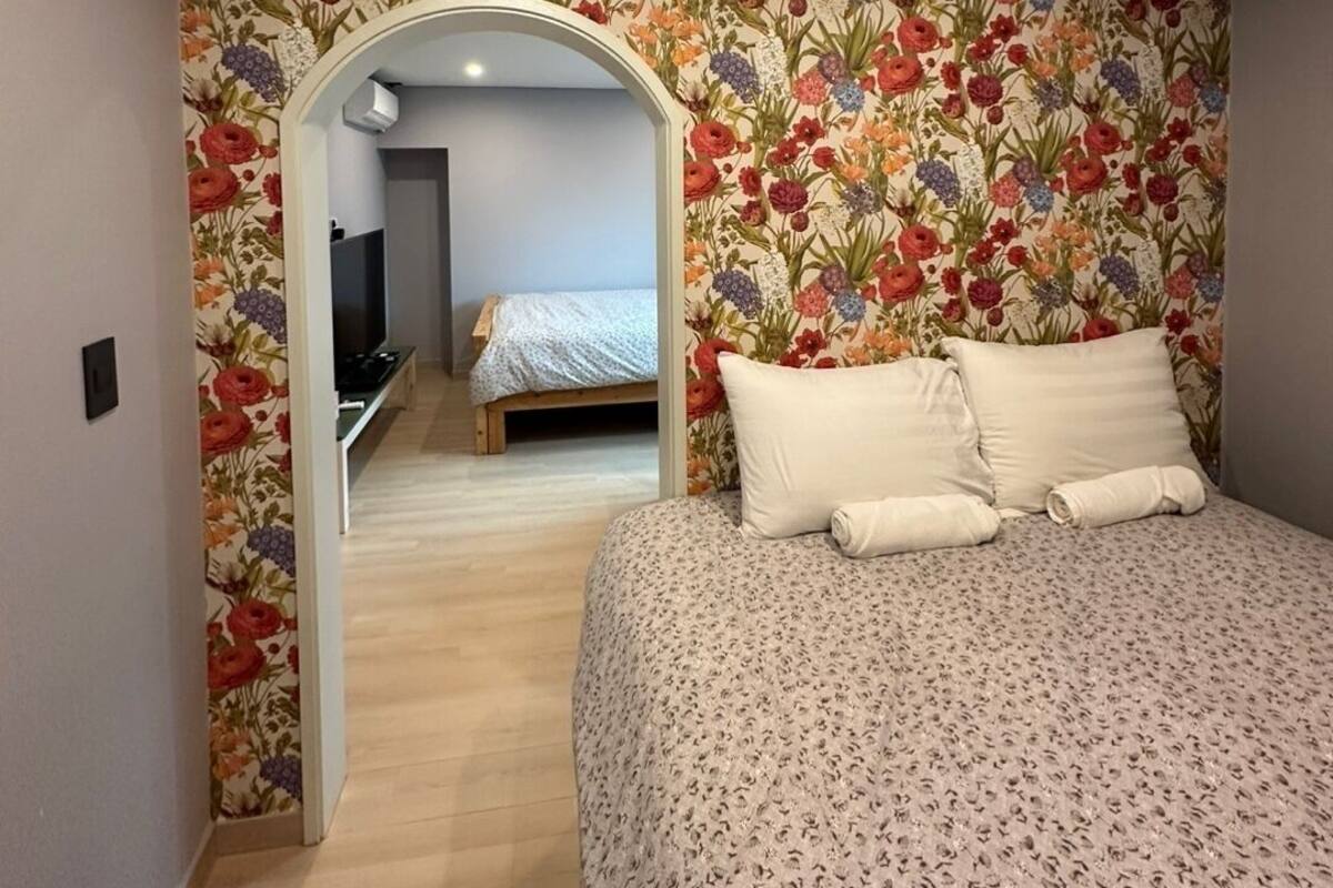 A bedroom with a floral wallpaper, a bed with white bedding, and a TV in the corner.