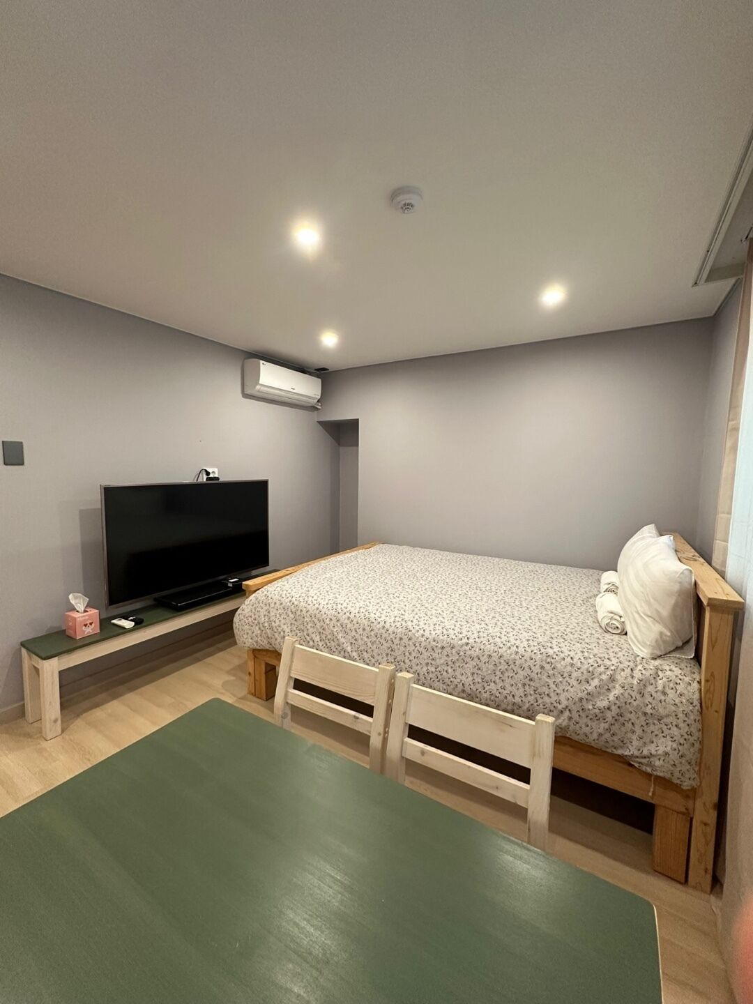Une chambre avec un lit, une télévision, une petite table et un tapis vert.