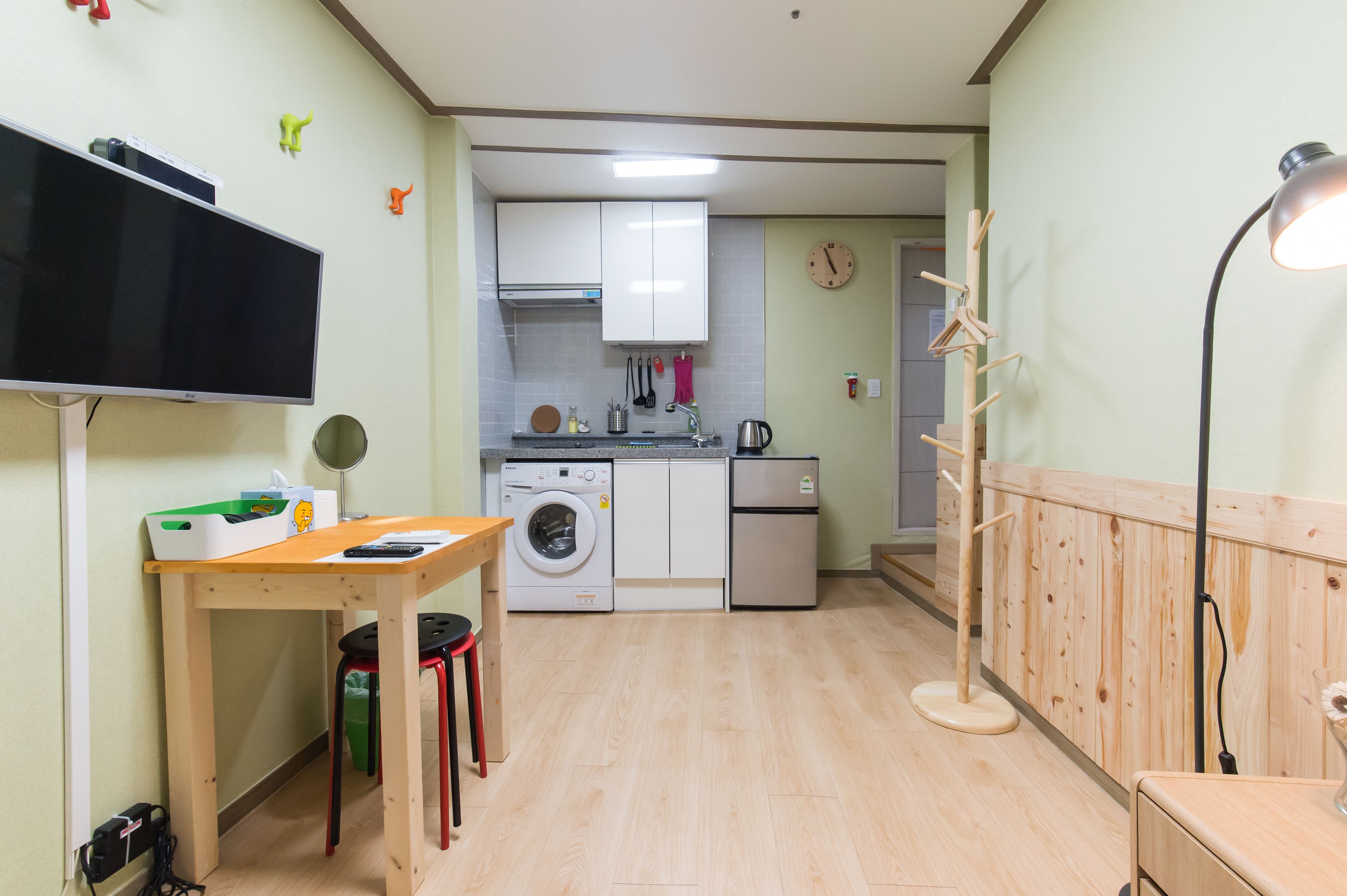 A compact kitchen with a washing machine, a small refrigerator, and a wooden table with a chair.
