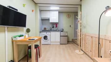 A compact kitchen with a washing machine, a small refrigerator, and a wooden table with a chair.