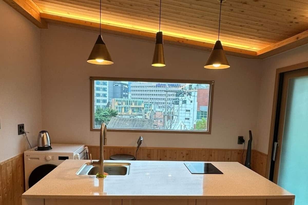 A modern kitchen with a central island, pendant lighting, and a view of the city through a large window.
