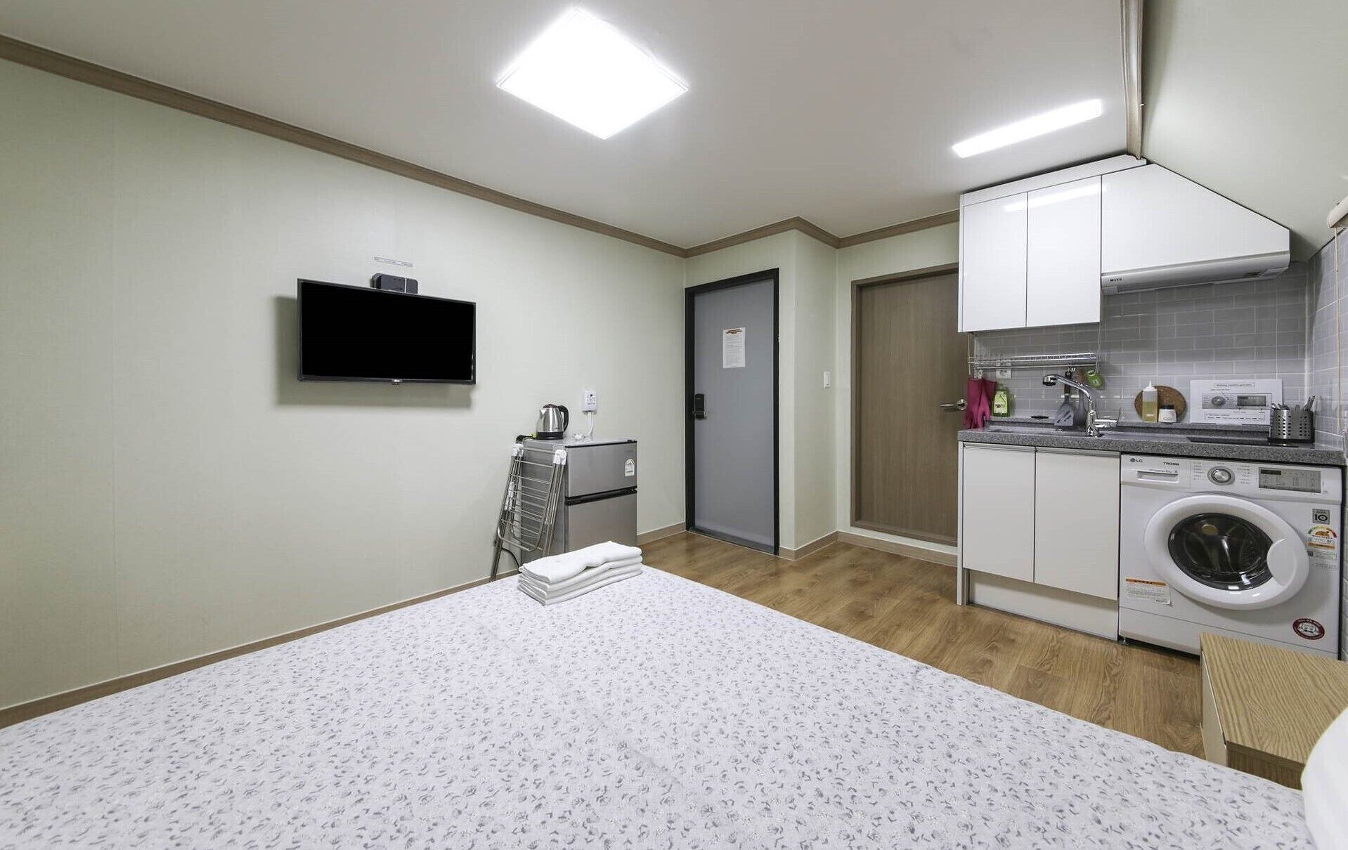 Habitación de hotel compacta con cama, televisión, lavadora y kitchenette.