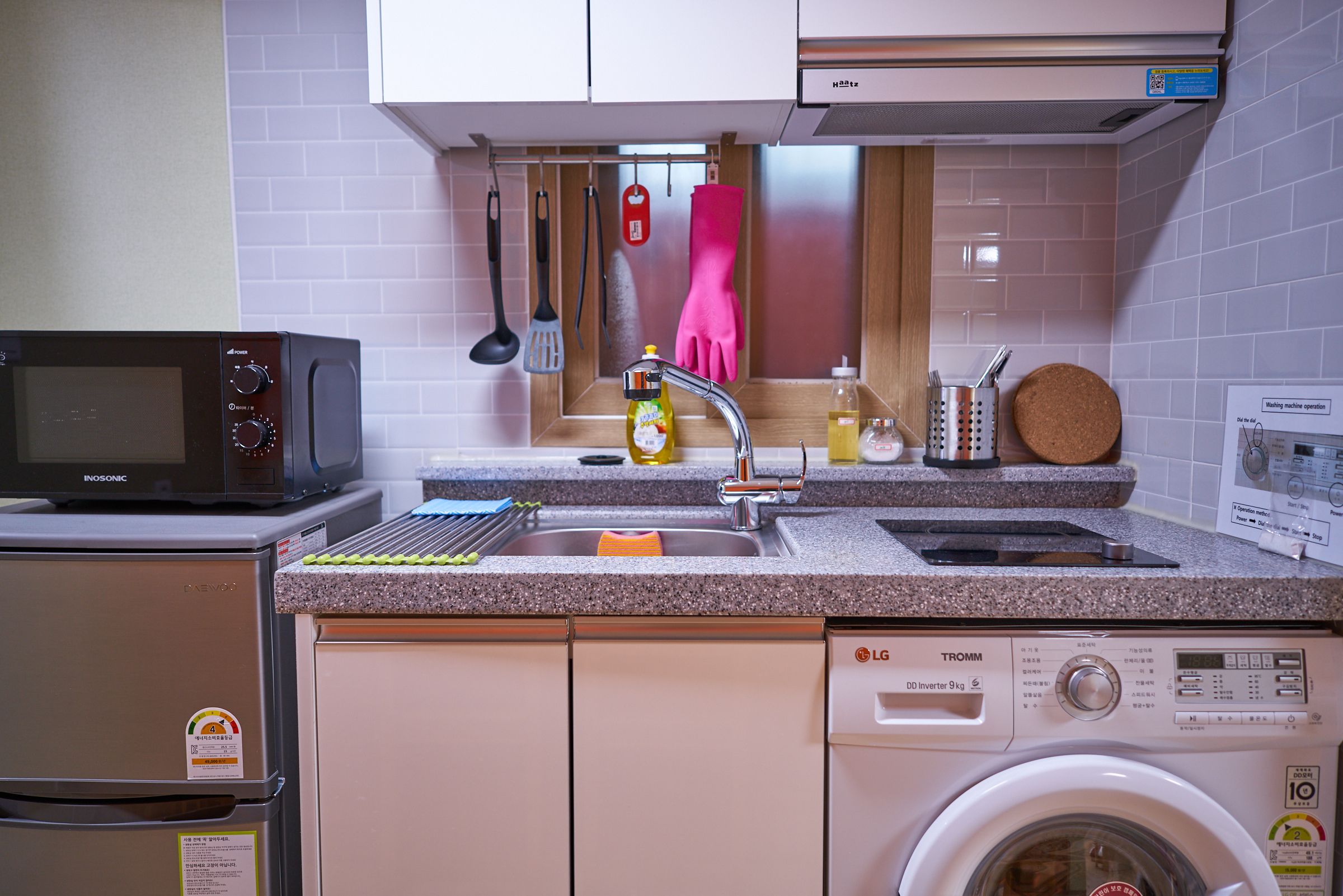 A compact kitchen with a microwave, refrigerator, sink, and washing machine.