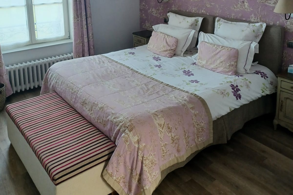 Un dormitorio con una cama grande, un banco, una ventana y un radiador.