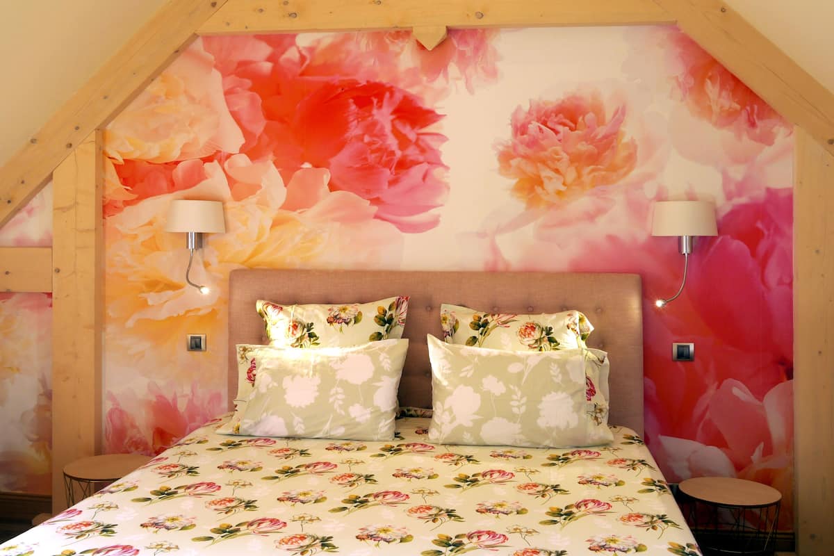 Un dormitorio con papel tapiz floral, techo de madera, dos lámparas de noche y una cama con ropa de cama floral.