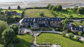 Un grand bâtiment à plusieurs étages, doté d’une toiture symétrique, entouré de pelouses verdoyantes et d’arbres.