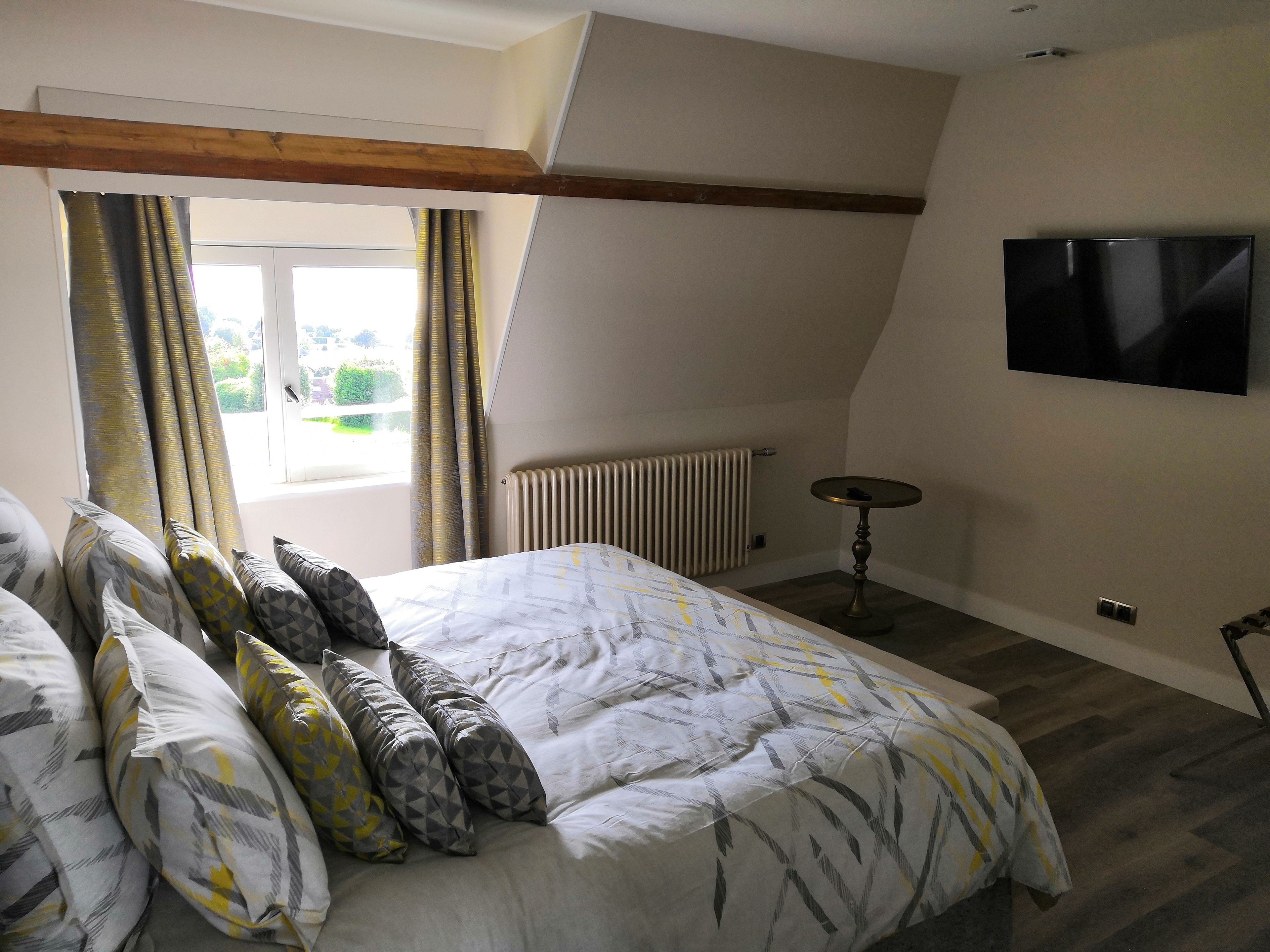 A bedroom with a large bed, a TV mounted on the wall, and a window with curtains.