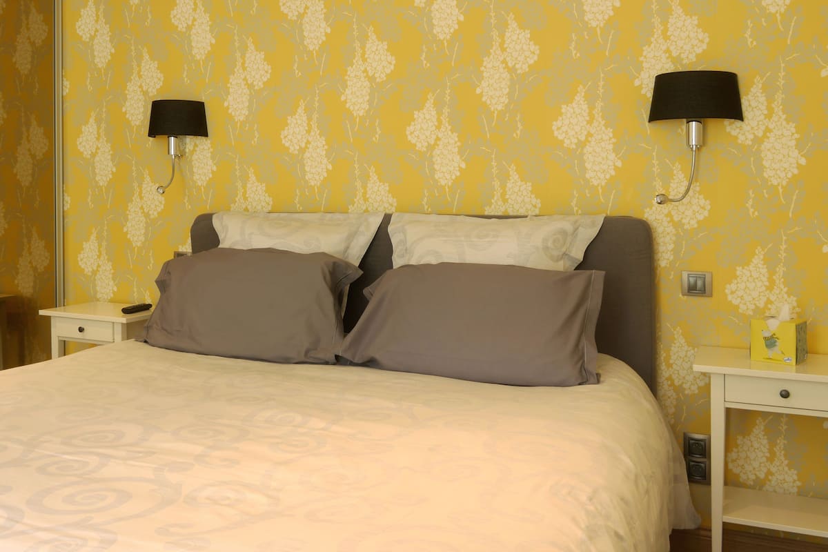 Una habitación de hotel con una cama, dos mesitas de noche y dos lámparas de pared.