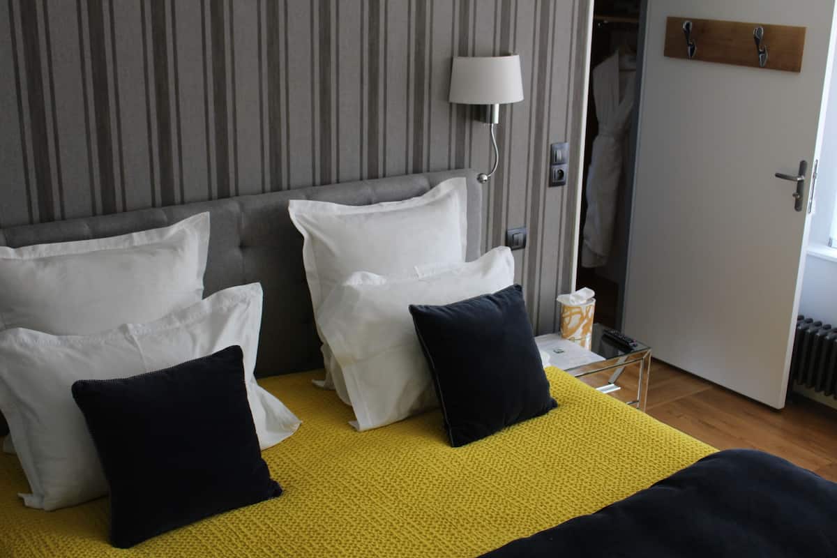 Una habitación de hotel con cama, almohadas, una lámpara de noche y una puerta de madera.
