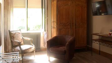 Une pièce comprenant une armoire en bois, un fauteuil en cuir, une chaise ancienne, un radiateur et un téléviseur posé sur un meuble en bois.
