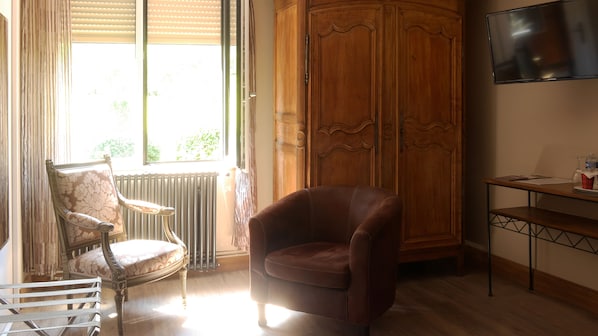 A room with a wooden wardrobe, a leather armchair, a vintage chair, a radiator, and a television on a wooden stand. - Domaine du Clos Fleuri (Honfleur)