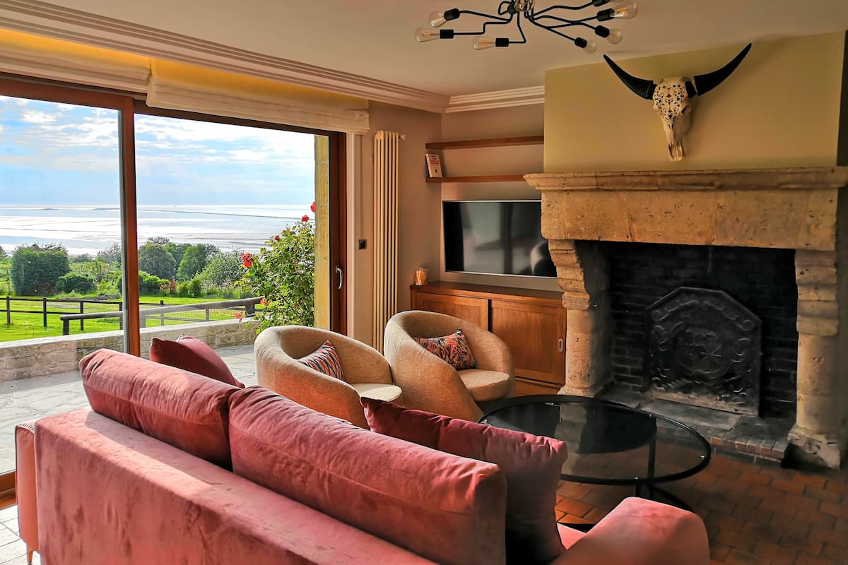 Una sala de estar con chimenea, televisión y vistas al océano.