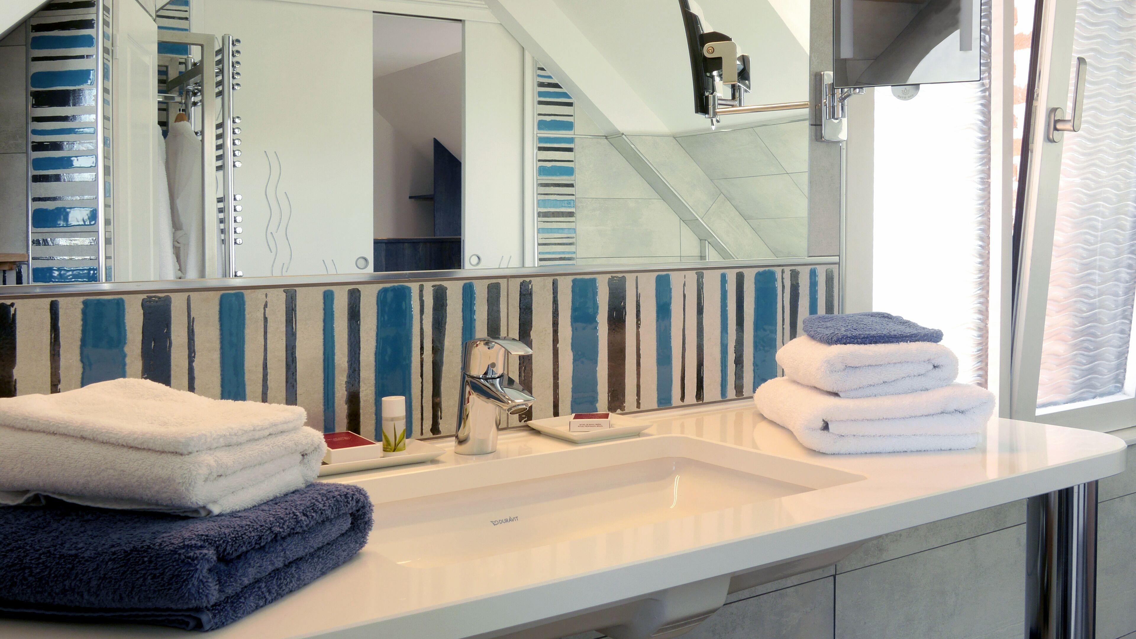 Un bany modern amb un mirall gran, un lavabo blanc i un suport per tovalloles.