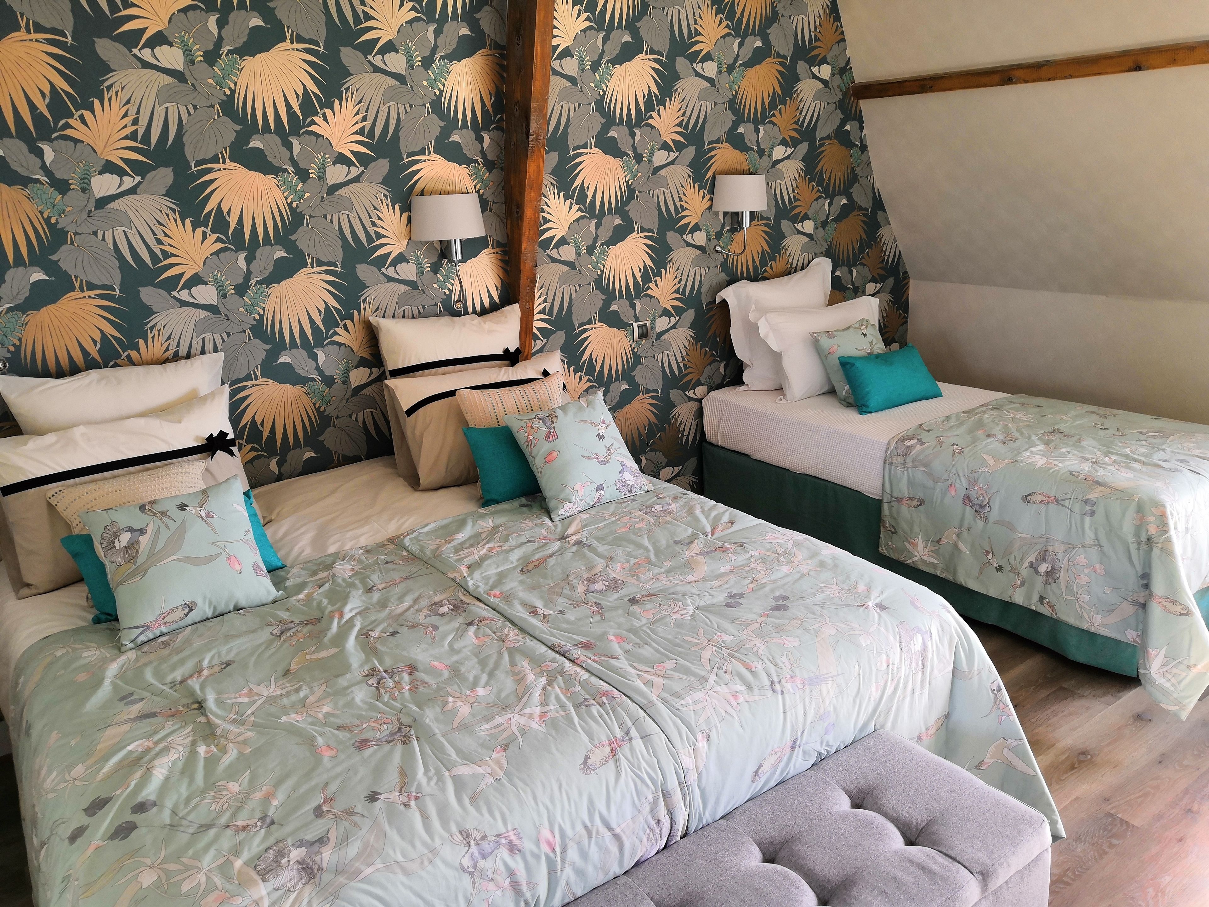 Une chambre avec deux lits, chacun agrémenté de draps à motifs floraux et de plusieurs oreillers. On y trouve deux lampes de chevet et une tête de lit en bois.
