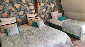 Une chambre avec deux lits, chacun agrémenté de draps à motifs floraux et de plusieurs oreillers. On y trouve deux lampes de chevet et une tête de lit en bois.